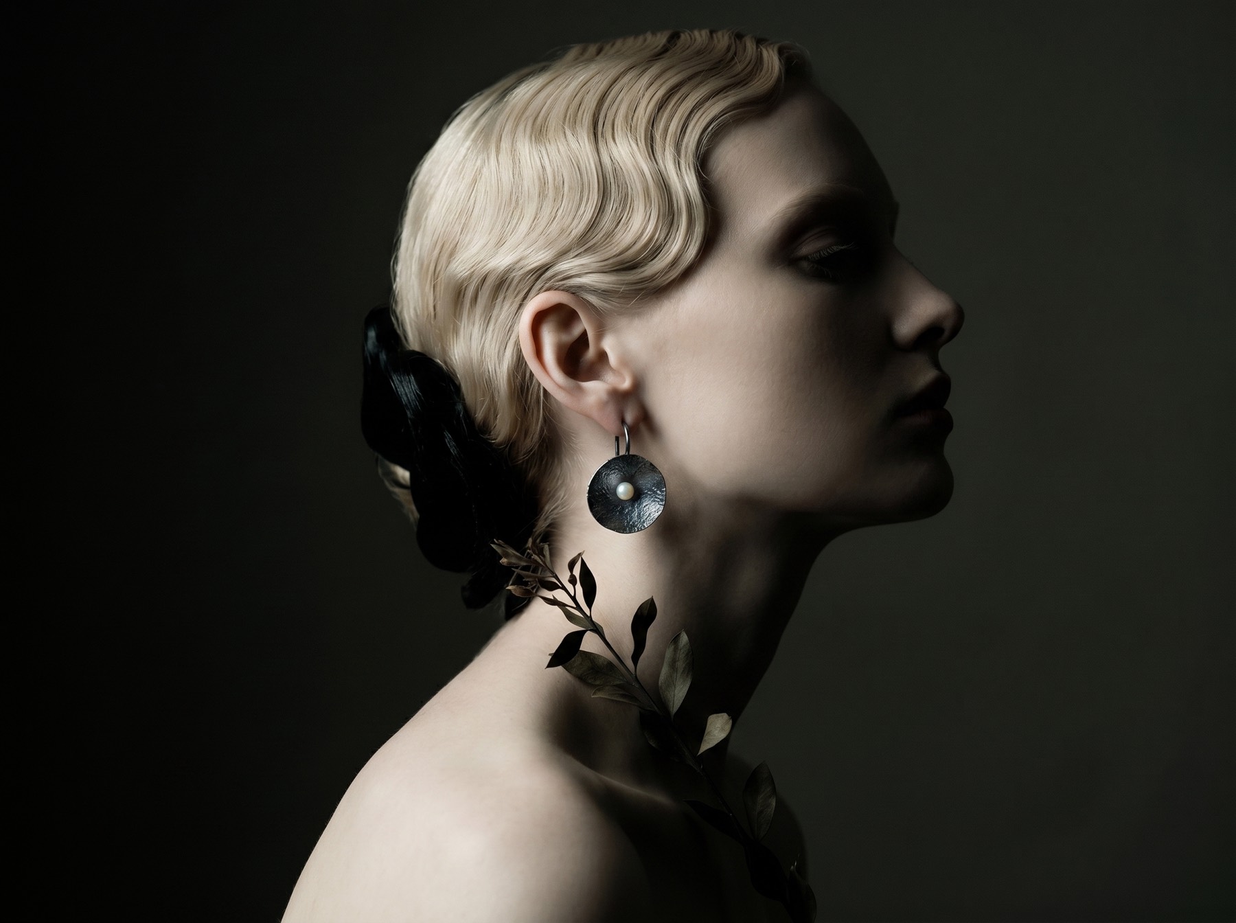 A profile portrait wearing a hammered disc earring holding a single pearl.
