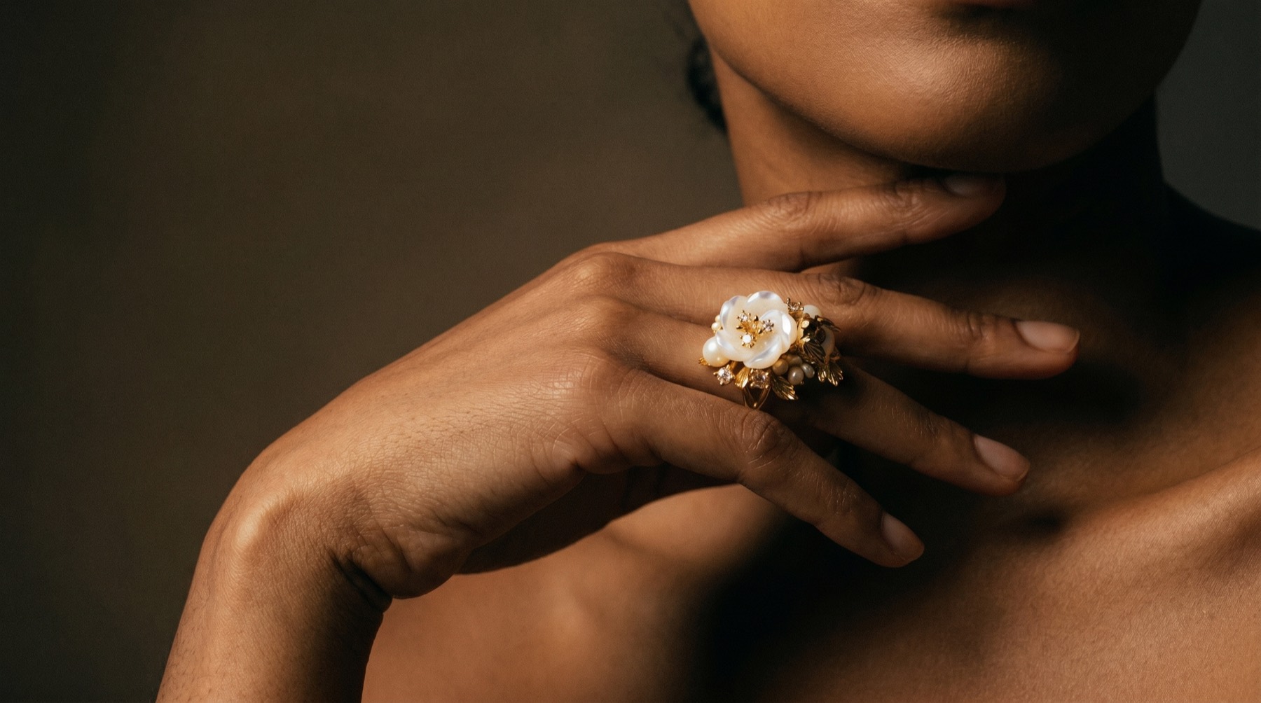 A hand wearing the Blossom Eternelle pearl-and-gold ring, held against warm light.