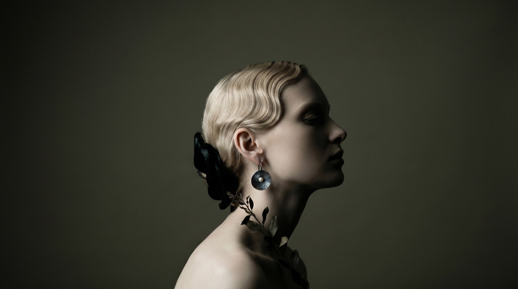 A wide olive-toned profile portrait with a pearl earring.